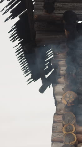 white smoke rises up in front of wooden house with burnt roof. cooking in log cabin yard. traditional architecture of middle ages under grey sky