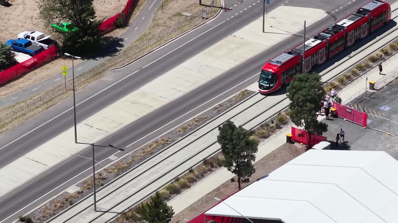 Inquadratura aerea con drone dall'alto che mostra un tram elettrico rosso in viaggio sui binari accanto a un tendone bianco.