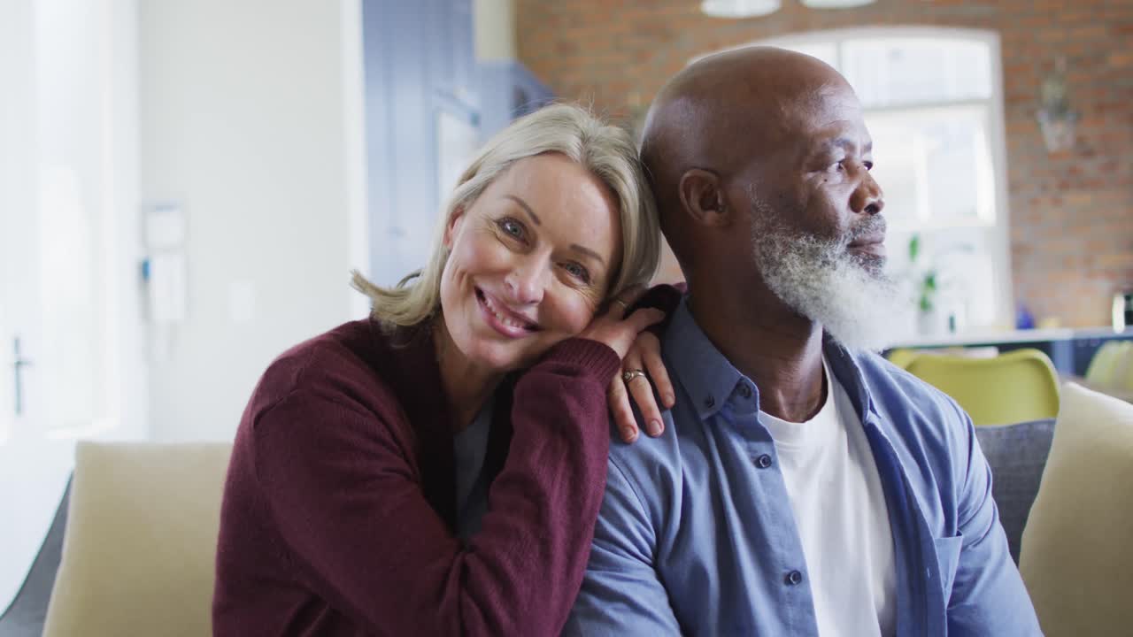 portret van een gelukkig ouder diverse echtpaar in de woonkamer zittend op de bank, omhelzend en glimlachend