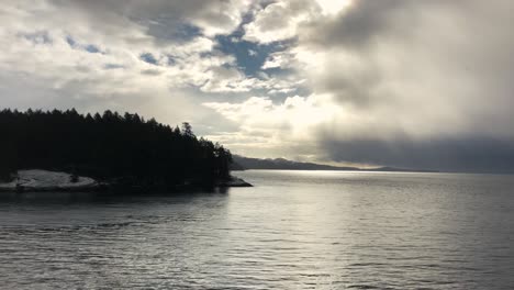 Felsige-Graue-Insel-Mit-Grünen-Bäumen-Im-Trincomali-Kanal-Mit-Einem-Riesigen-Regenschauer-Im-Hintergrund-An-Einem-Bewölkten,-Regnerischen-Tag-In-Kanada