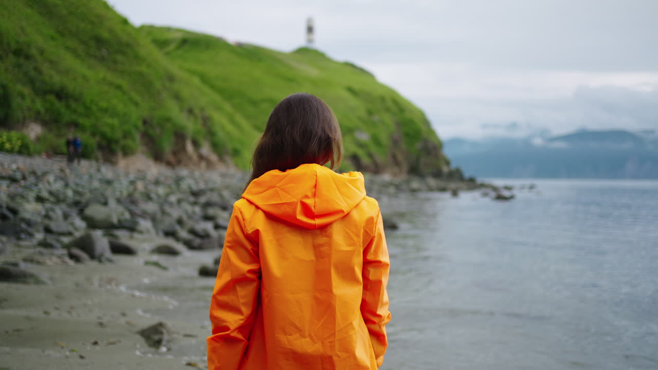 Woman in Orange Jacket at Beach, Looking at Ocean