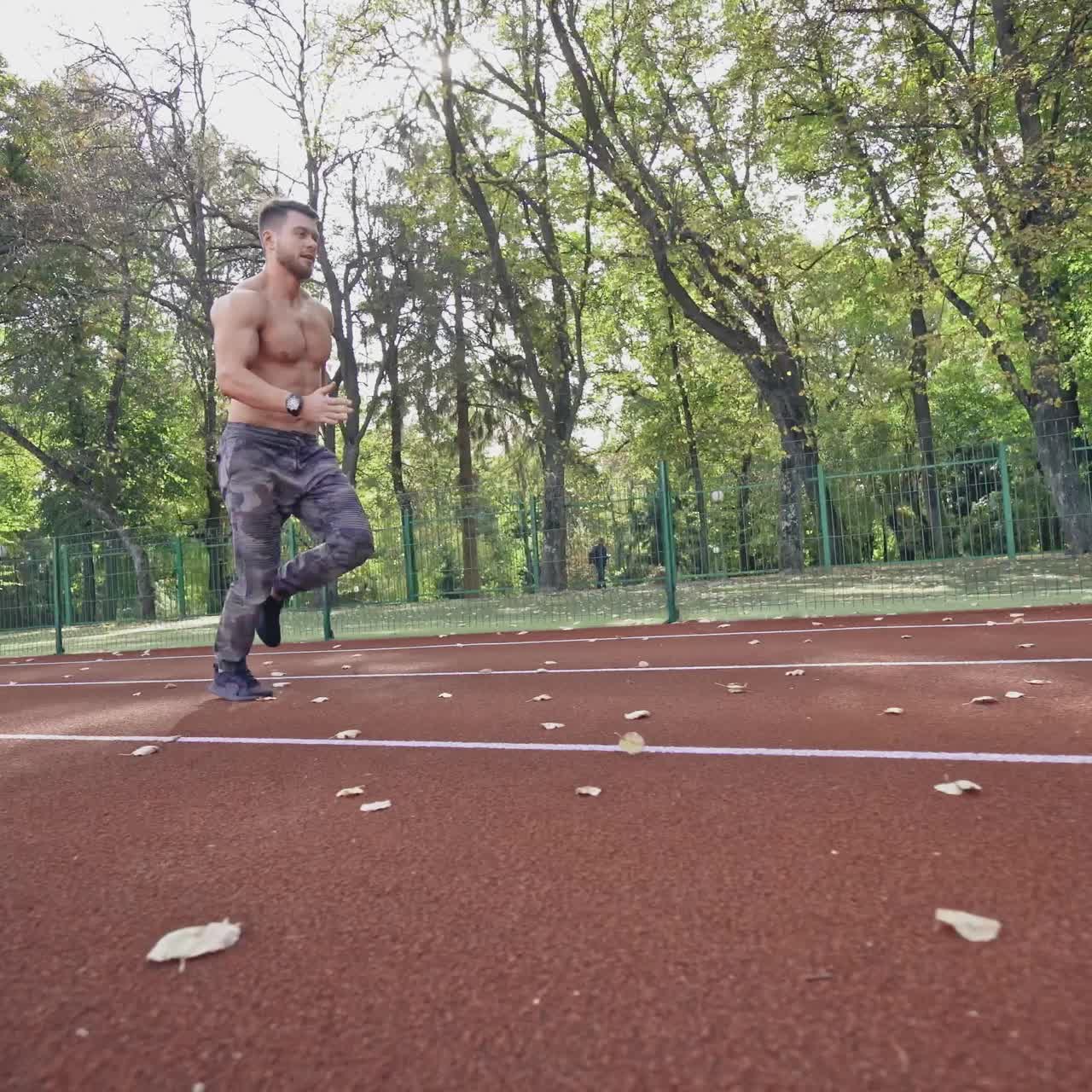 Shirtless runner training on the stadium. Strong athlete is running in the park at sunny day. Healthy lifestyle. Slow motion.