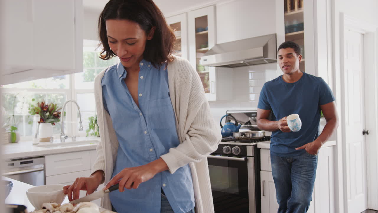 Young African American woman preparing food in the kitchen, her partner standing behind talking
