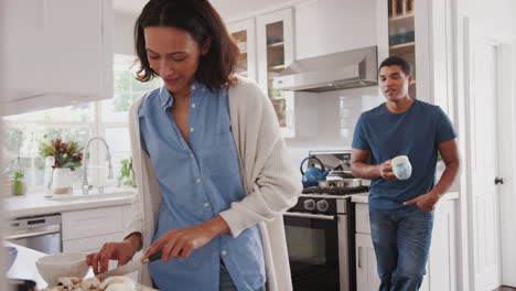 Una-Joven-Afroamericana-Preparando-Comida-En-La-Cocina,-Su-Pareja-Detrás-Hablando