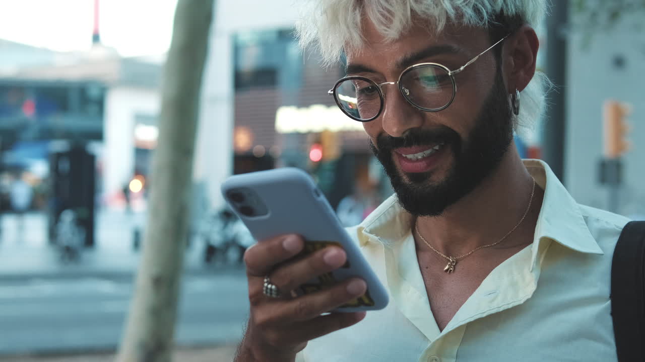 Giovane uomo che sorride mentre usa lo smartphone all'aperto in città