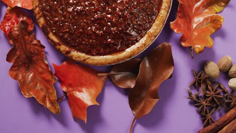 video of autumn leaves, spices and pie on purple background