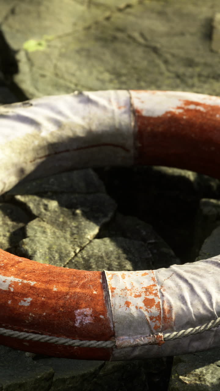 Life buoy resting on cracked stones by the water at sunset