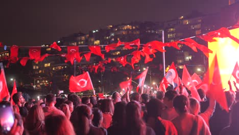 large crowd of people waving turkish flags at a night event