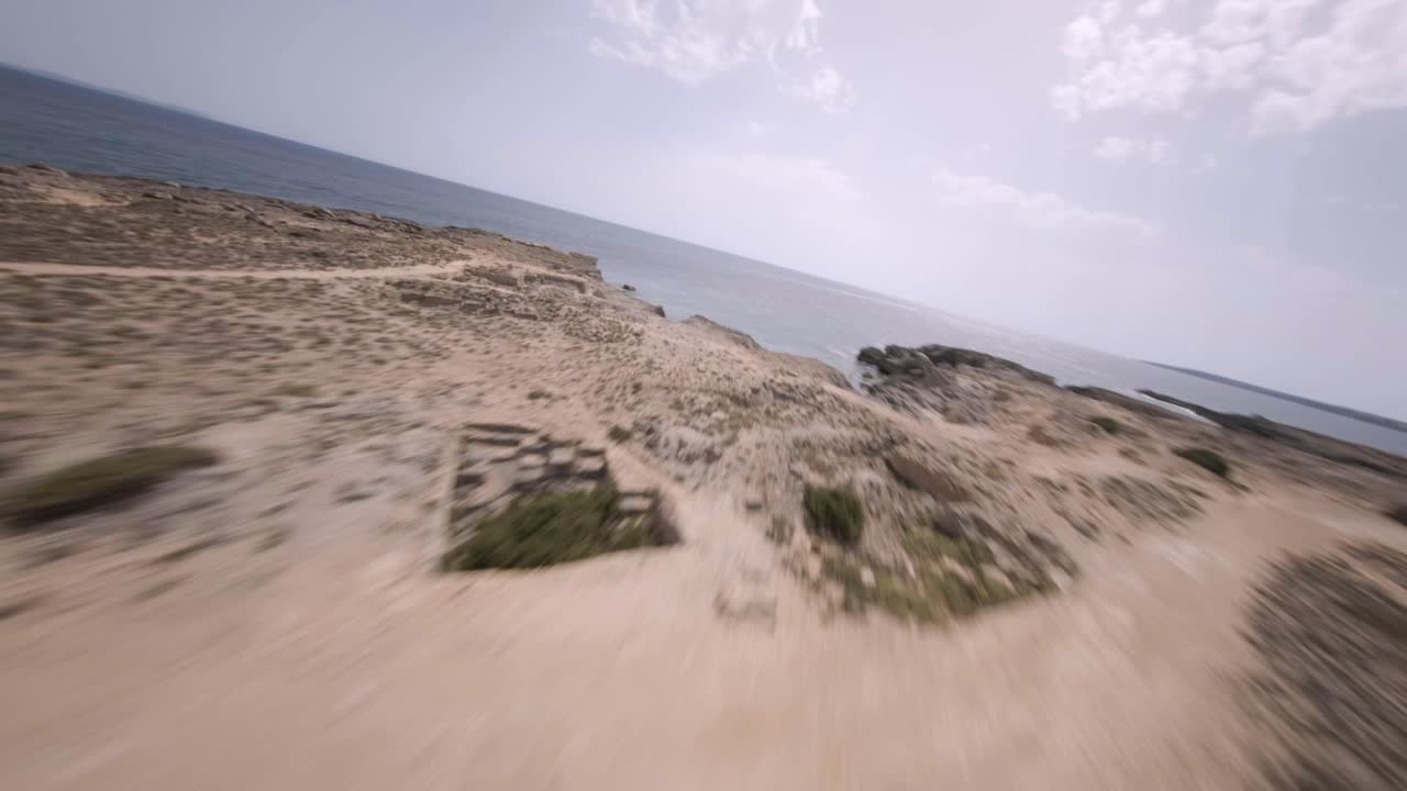 fpv drone hacia adelante tiro en movimiento volando sobre las playas rocosas de faro de s'estalella en mallorca, islas baleares, españa en un día soleado