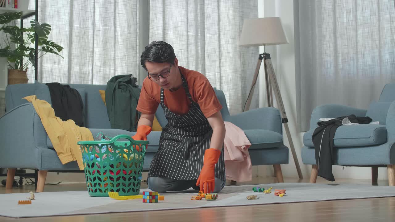 피곤 한 아시아 남성 집주인 은 장난감 에서 망진창 한 방 을 청소 하는 동안 머리 를 흔들고 있다