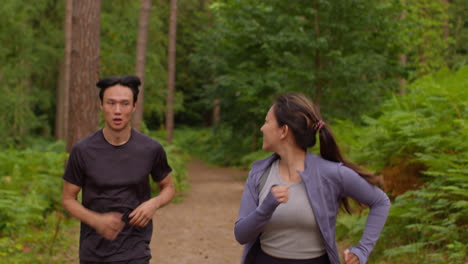 mid adult couple exercising doing work out outdoors running through forest with woman encouraging tired man wearing sports clothing