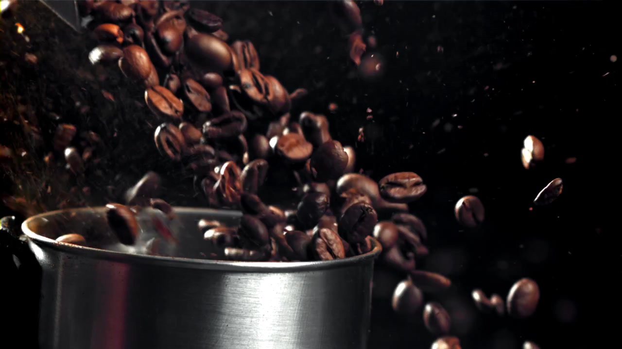 Ristede kaffebønner falder ned i en metalkande i slowmotion