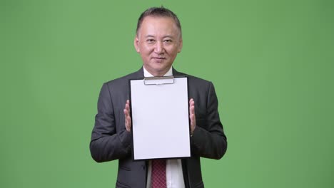 mature japanese businessman showing clipboard at camera