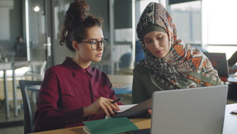 Businesswoman-Discussing-Papers-with-Female-Colleague-in-Hijab