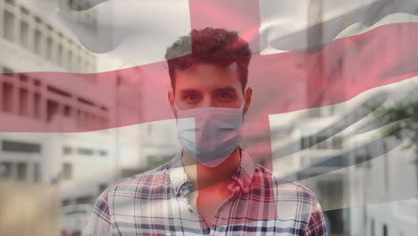 animation of flag of england over latin man wearing face mask in city street