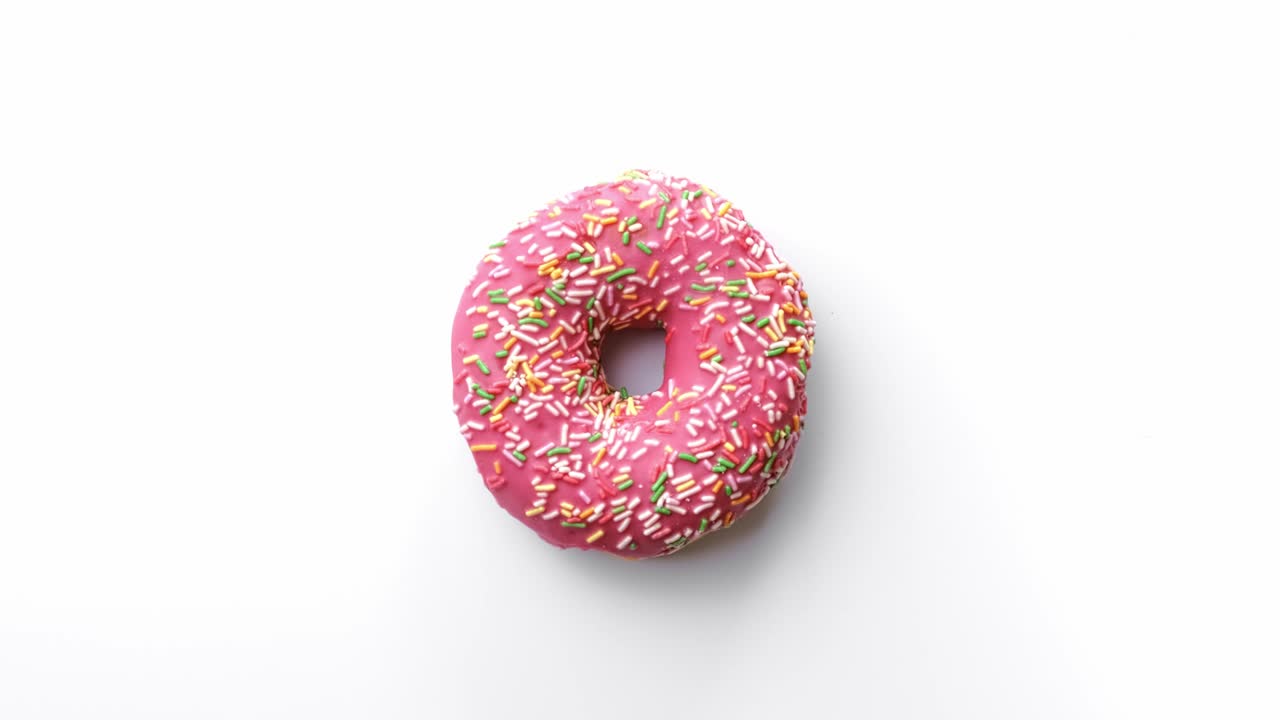 vista superior rosquilla fresca con esmaltes rosados y salpicaduras multicolores que se vuelven aisladas en blanco