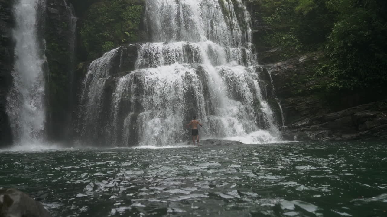 Campo lungo con panoramica verso l'alto su un uomo alla base delle cascate Nauyaca in Costa Rica