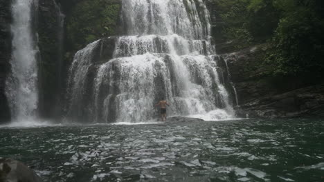 wide shot panning up to man at base of nauyaca waterfalls in costa rica