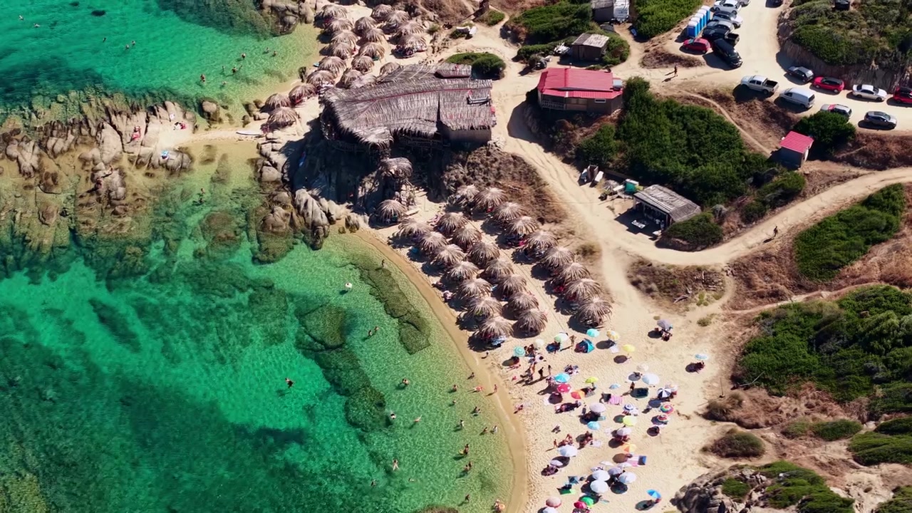 Ripresa con drone di un bar sulla spiaggia, ombrelloni e persone sulla riva sabbiosa in Grecia durante la stagione estiva