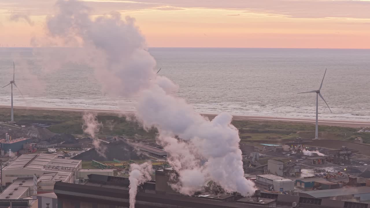 Panorama al tramonto con ciminiere di fabbriche e fumo in un distretto industriale.