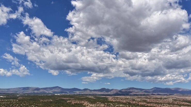 Timelapse de dron 4K se inclina hacia arriba para capturar gigantes formaciones de nubes moviéndose sobre un vasto horizonte suroeste. El movimiento cinematográfico de ángulo bajo revela nubes masivas desplazándose sobre las crestas de las montañas del desierto.