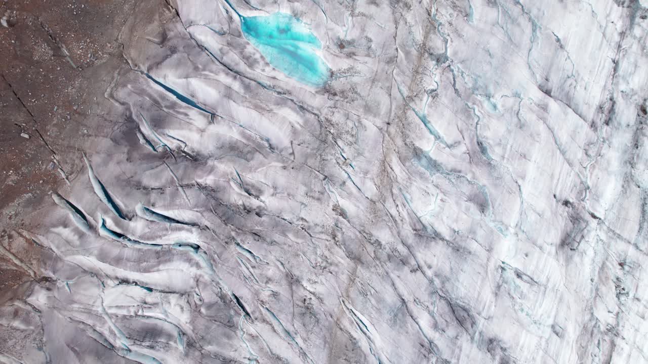 Ilmakuva dronella, 4k-lähikuva Aletschin jäätiköstä, esitellen säröillä olevaa jäätä, railoja ja sinisiä sulamisvesialtaita, korostaen jäätikön tekstuuria ja ilmastonmuutoksen näkyviä vaikutuksia Sveitsin Alpeilla.