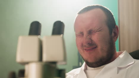 una vista de cerca de un técnico sonriendo mientras examina muestras a través de un microscopio en un laboratorio