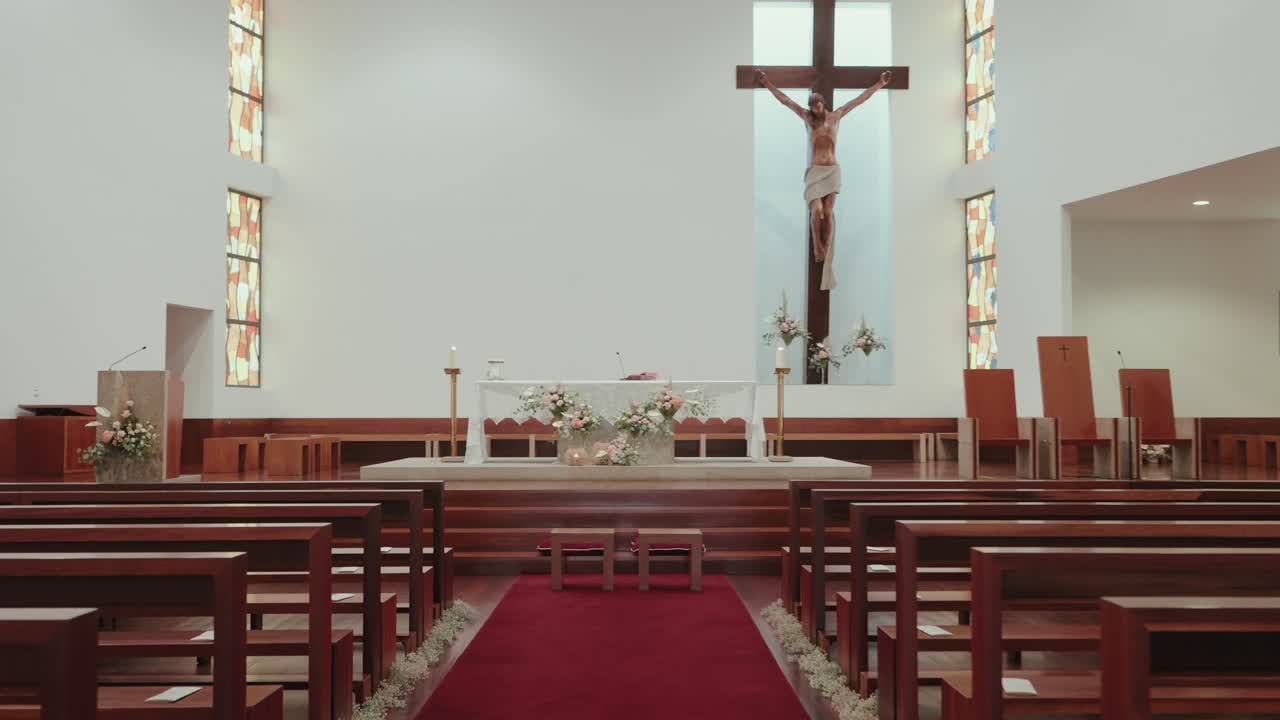 Elegant church setup featuring a red carpet aisle, floral decorations, and a crucifix above the altar creating a serene and sacred atmosphere for a wedding
