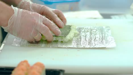 cu cocinero en cámara lenta está preparando un rollo japonés se extiende en el tapete de algas nori con arroz al vapor