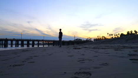 un hombre en silueta solo en la playa en el muelle stearns wharf al atardecer mirando el océano en la arena en santa barbara, california