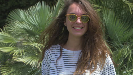 mujer joven con gafas de sol sonriendo y riendo en un entorno tropical