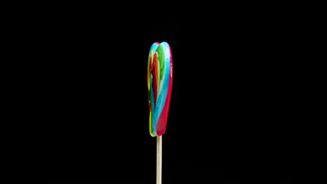 caramel lollipop heart multicolored on a stick spinning on a black background. candy cane spiral copy space