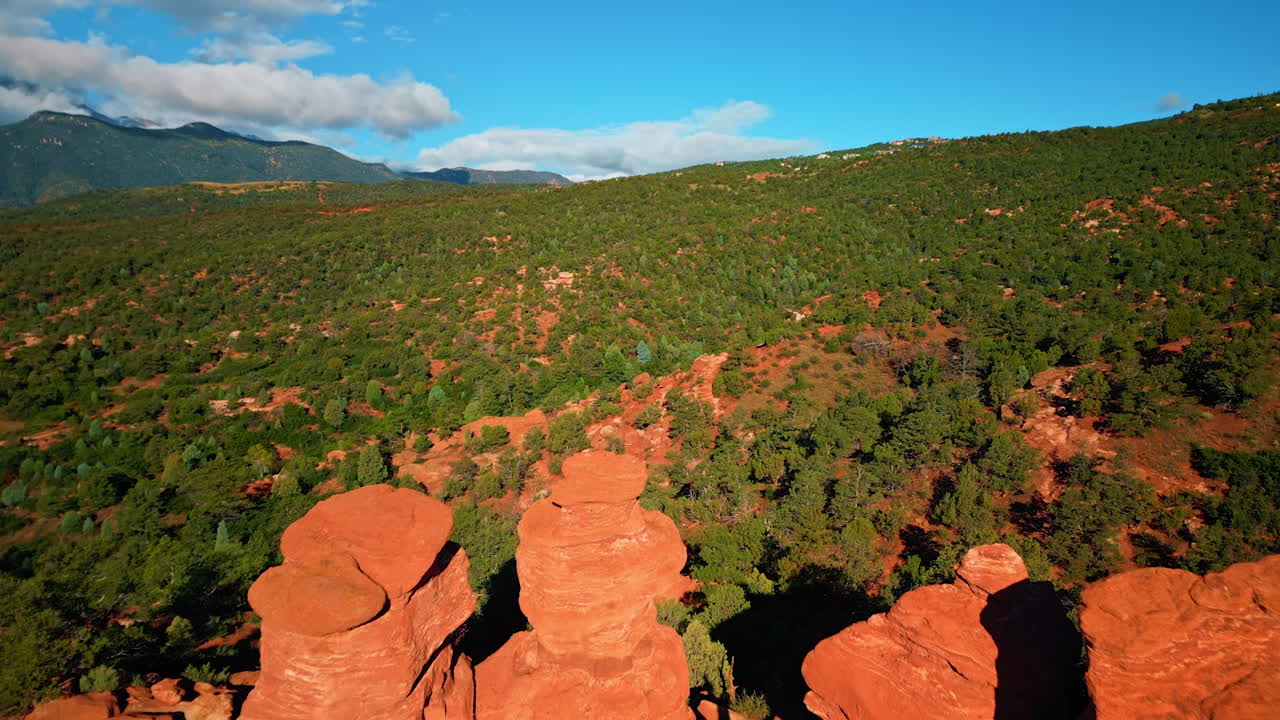 Flagstaff, USA, 24 August 2025: Woman wearing black shirt and white pants stands dancing on the red rocks. Green trees and bushes cover the landscape of Garden of the Gods Park, Colorado Springs, Colorado, USA