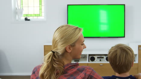 Vista-Trasera-De-La-Familia-Sentada-En-Un-Sofá-En-El-Salón-Viendo-La-Televisión.