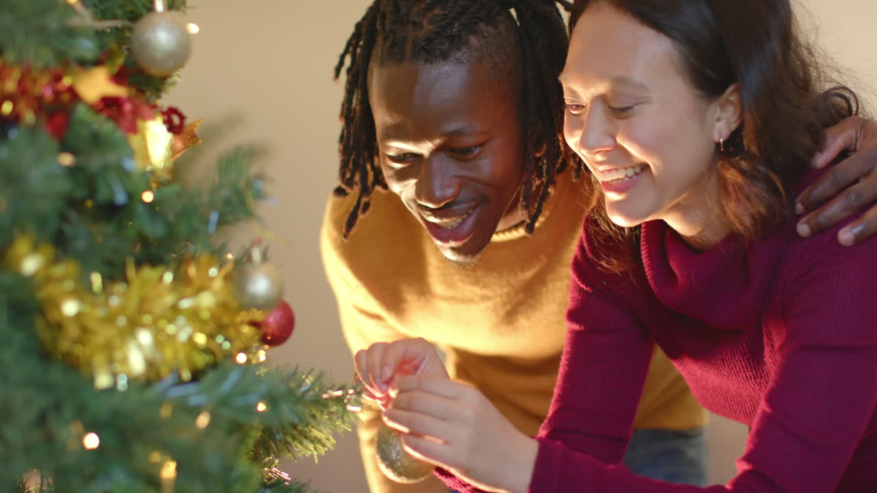 una pareja feliz decorando el árbol de navidad en casa, en cámara lenta.