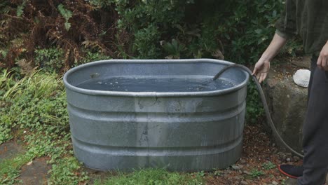 Caucasian-man-putting-a-hose-inside-an-exterior-bathtub-for-cold-plunging