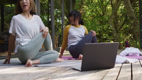 asian mother and daughter practicing yoga outdoors in garden with laptop