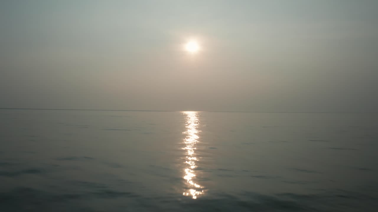 Drone glider hen over en tåget kystlinje og afslører solens stråler på det rolige vand, der strækker sig mod den endeløse horisont ved Kudle Beach i Gokarna, Indien, under solnedgangen
