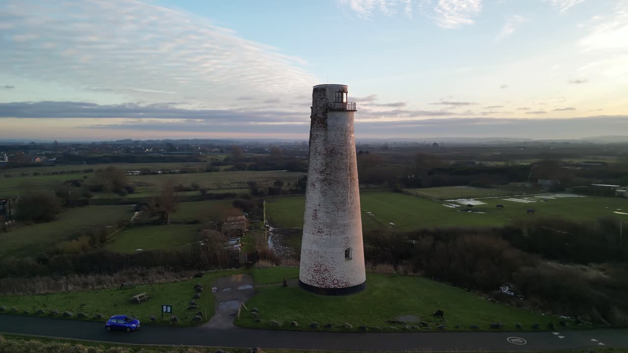 Beautiful aerial drone slow clockwise pan of Leasowe Lighthouse revealing sunset at dusk in winter, UK