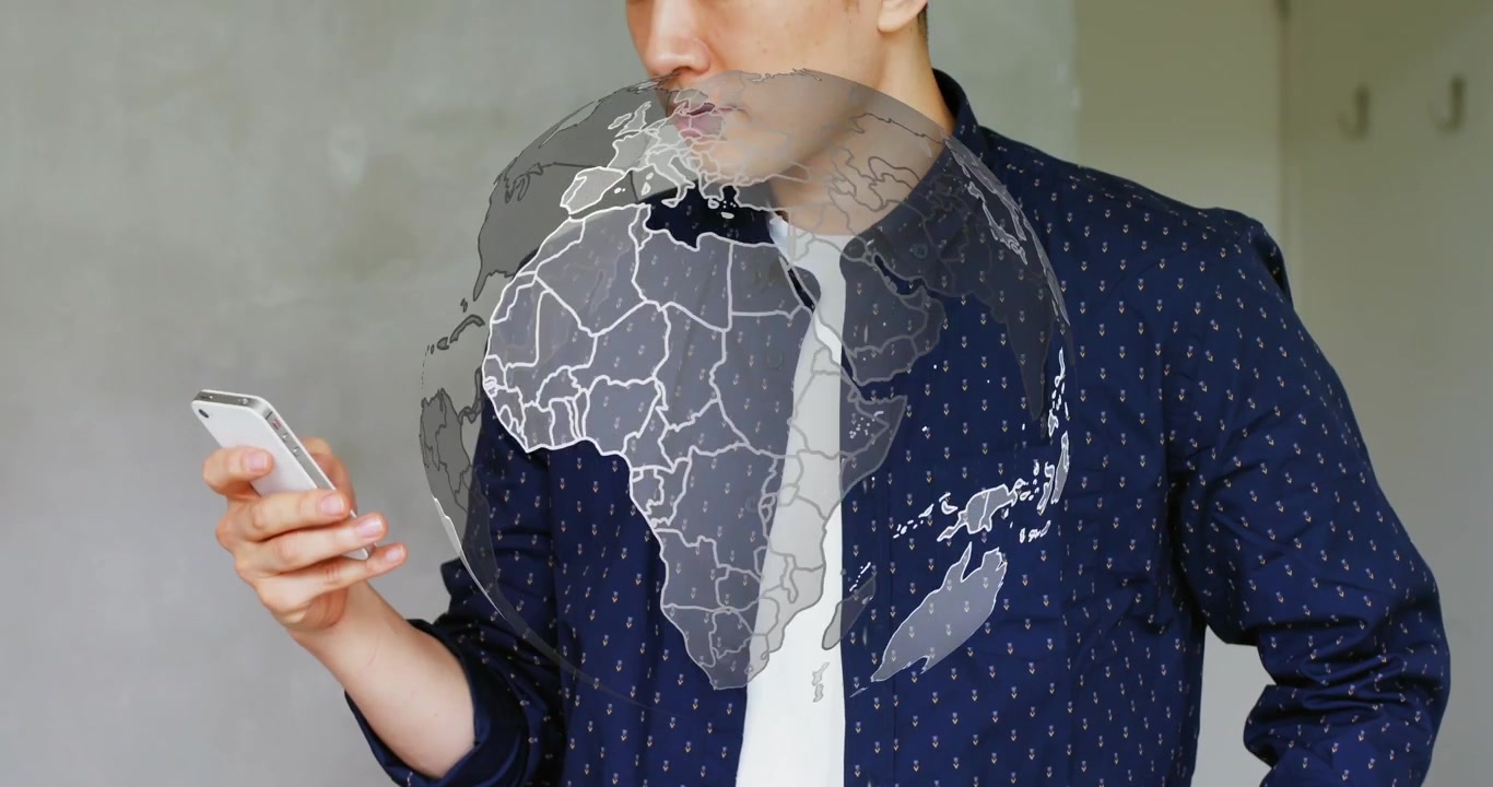 Uomo asiatico con maglia blu scuro che reagisce a un globo olografico che appare, legge il telefono e tiene dei piani arrotolati, in studio