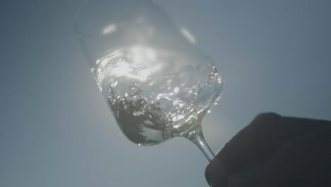 toma en cámara lenta de la mano agitando vino blanco en vidrio transparente que refleja la luz del sol
