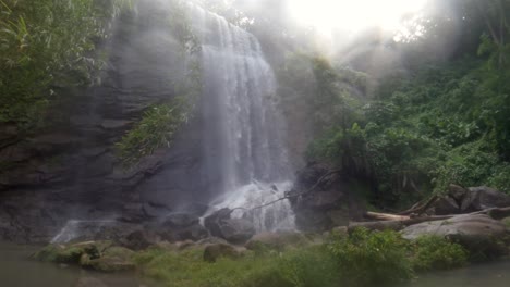 Ein-Wasserfall-Im-Dschungel-Mit-Dichtem-Nebel,-Der-Im-Wind-Weht-Und-Die-Sonne-Am-Himmel-Scheint