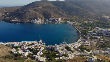slow orbit drone footage of katapola village and port in amorgos, capturing whitewashed houses and anchored boats in calm aegean waters