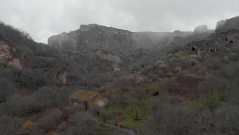 aerial view of rural armenia showing two people walking near a house with the khndzoresk caves in the background the scene captures natural beauty and historical elements of the region