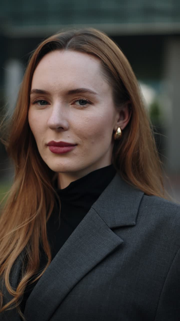 A confident Caucasian businesswoman keeps looking directly at the camera at outdoor business office terrace at sunset, captured in a close-up parallax shot
