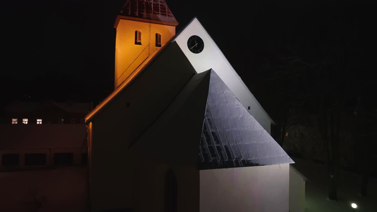 Ascensão aérea em frente à igreja iluminada de Rakvere, noite de inverno na Estônia.