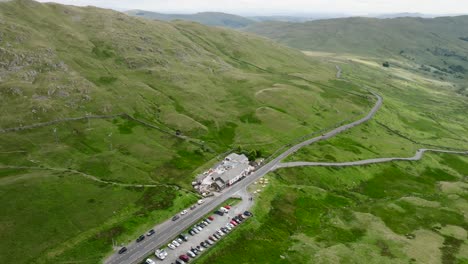 the kirkstone pass summit and inn from altitude with pan showing valley and lake windermere. busy car park. summer. lake district, cumbria, uk