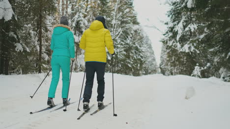 Ein-Mann-In-Einer-Gelben-Jacke-Und-Eine-Frau-In-Einem-Blauen-Overall-Im-Winter-Im-Wald-Beim-Skifahren-In-Zeitlupe.-Rückansicht.-Zurück