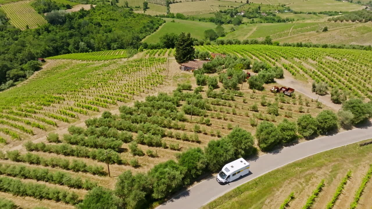 Aerial view of a camper van driving in middle of summer green vineyards of Italy