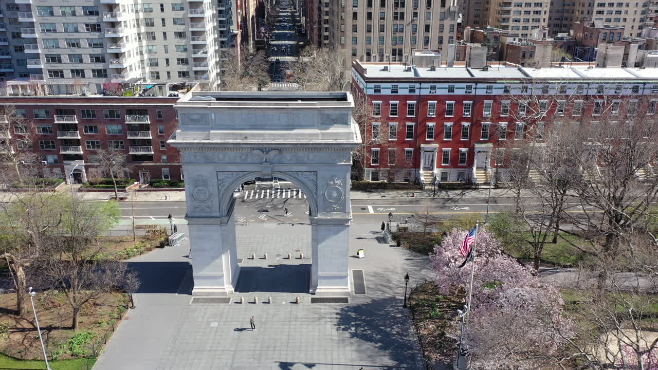 An aerial day time view over Washington Sq. Park looking up Fifth Avenue. The drone dolly in to the Washington Square Arch in NYC. The park is empty - the Empire State Building is in the distance.